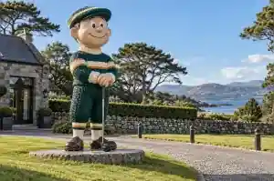 2.2 m cartoon golfer figure standing on a grass verge beside a golf club driveway in St Andrews, Scotland