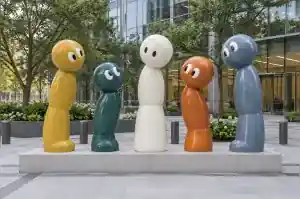 Five cartoon abstract character sculptures in different flat colours standing as a group on a Rotterdam corporate plaza
