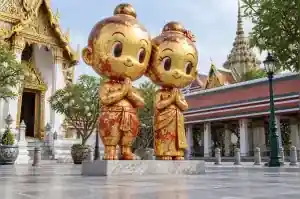 Gold leaf cartoon couple sculpture in a Bangkok temple courtyard with patchy hand-laid gold