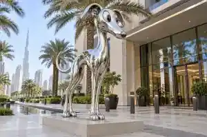 Detail of the curving chrome-finish head of a cartoon whippet sculpture reflecting palm trees