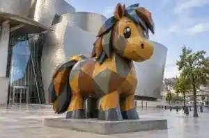 Three-quarter view of a 2.4 m cartoon pony sculpture built from flat angular planes in earth tones