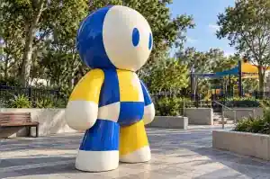 Three-quarter view of a large colour-blocked abstract character sculpture on a public plaza